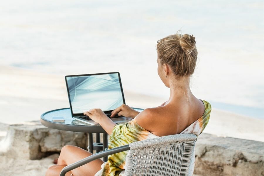 Frau verdient mit Laptop am Meer Geld